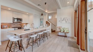 A modern kitchen with a central island, bar stools, and a staircase leading to a loft area.