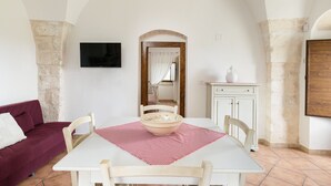 A dining area with a table, chairs, a bowl, a television, and a doorway leading to another room.