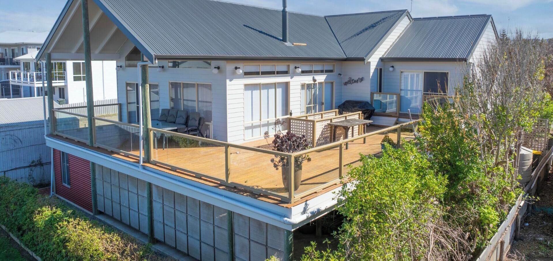 Une maison à deux étages dotée d’un balcon, d’un espace extérieur aménagé et couvert, et d’un garage visible.