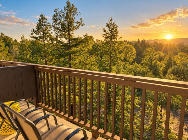 A balcony with a wooden railing overlooking a forested area during sunset.