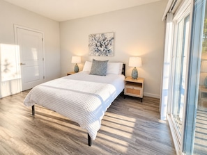A bedroom with a bed, two bedside tables, a nightstand, a wall-mounted artwork, and a large window. - Sonoma 2BR/2BA Condo | Full Kitchen, A/C & Views (Sonoma)