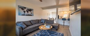 Spacious living room with L-shaped couch, smart TV, open kitchen, dining nook, and patio views