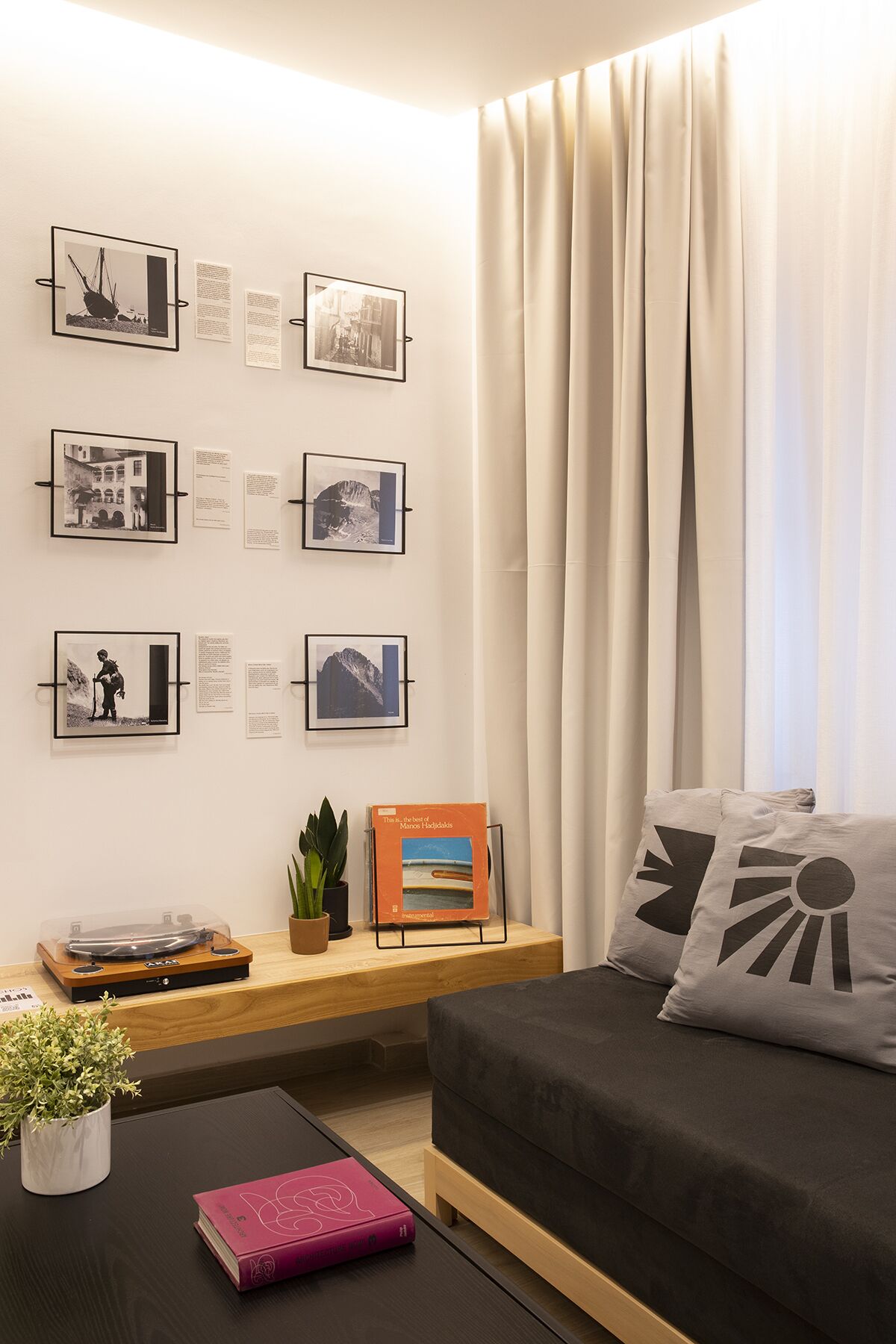 Ein modernes Wohnzimmer mit einer Couch, einem Couchtisch und einer Wand mit gerahmten Fotografien und Infotafeln.
