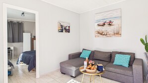 A modern living room with a grey sofa, a small round coffee table, and a painting of boats on the wall. - Pretty yellow-shutter house w/ terrace for 6 (La Tranche-sur-Mer)