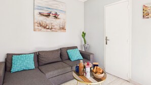 A living room with a grey sofa, a coffee table, a painting, a cactus, and a door. - Pretty yellow-shutter house w/ terrace for 6 (La Tranche-sur-Mer)