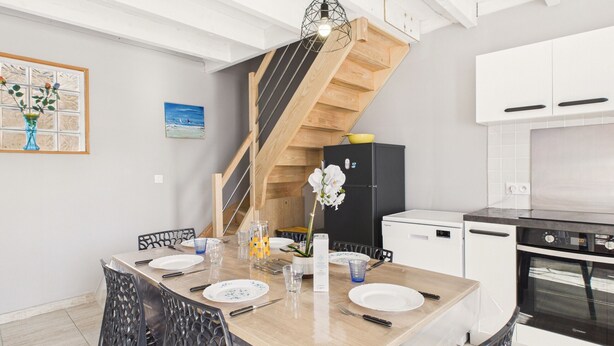 A modern kitchen with a wooden staircase, white cabinets, and a dining area with a wooden table and chairs. - Pretty yellow-shutter house w/ terrace for 6 (La Tranche-sur-Mer)