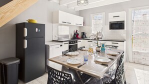 A modern kitchen with white cabinets, a black refrigerator, and a dining area with a table set for four. - Pretty yellow-shutter house w/ terrace for 6 (La Tranche-sur-Mer)