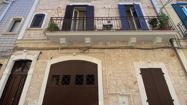 A multi-story building with a central entrance, large wooden doors, and a balcony with metal railings. - Racconti di pietra (Conversano)