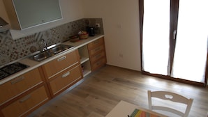 A kitchen with wooden cabinets, a sink, and a stove. There is a window with a view of the outside. - Racconti di pietra (Conversano)