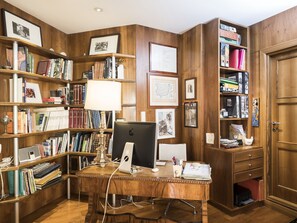 A wooden-paneled room with a desk, bookshelves, and framed pictures.