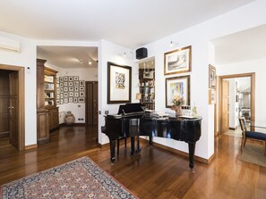 A spacious living room with a grand piano, a large rug, and a bookshelf filled with books and framed pictures.