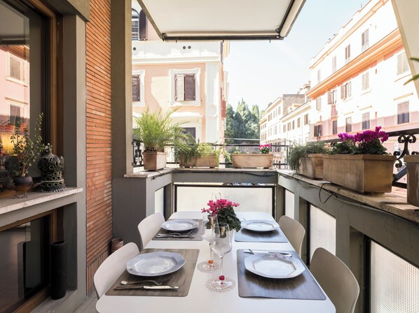 An outdoor dining area with tables set for two, potted plants, and a view of the cityscape.