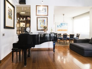 A living room with a grand piano, a dining area with chairs, and artwork on the walls.