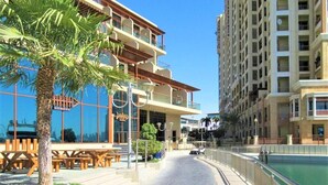 A modern hotel with a pool, outdoor seating, and a clear view of the surrounding buildings. - Luxurious Studio With Breath-taking Palm Views (Dubai)