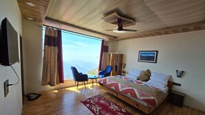Un dormitorio con cama, escritorio, silla, ventilador de techo y una ventana grande con vistas a las montañas.