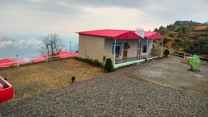 Un edificio pequeño con techo rojo y fachada blanca, rodeado por un área de grava y vistas a un paisaje montañoso.