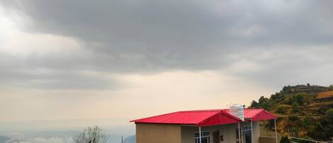 A building with a red roof, a covered porch, and a view of a hilly landscape.