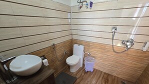 Un baño pequeño con suelo de madera, lavabo blanco, inodoro y zona de ducha.