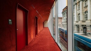 A hallway with red carpet, doors, and a view of a train passing by through large windows. - Met Boutique Hotel (Zagreb)