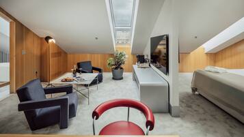 Una habitación de hotel moderna con comedor, una silla roja, un sofá, un televisor y una planta.
