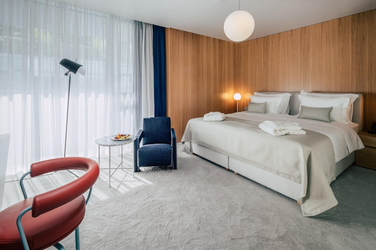 A hotel room with a bed, a chair, a small table, and a lamp.