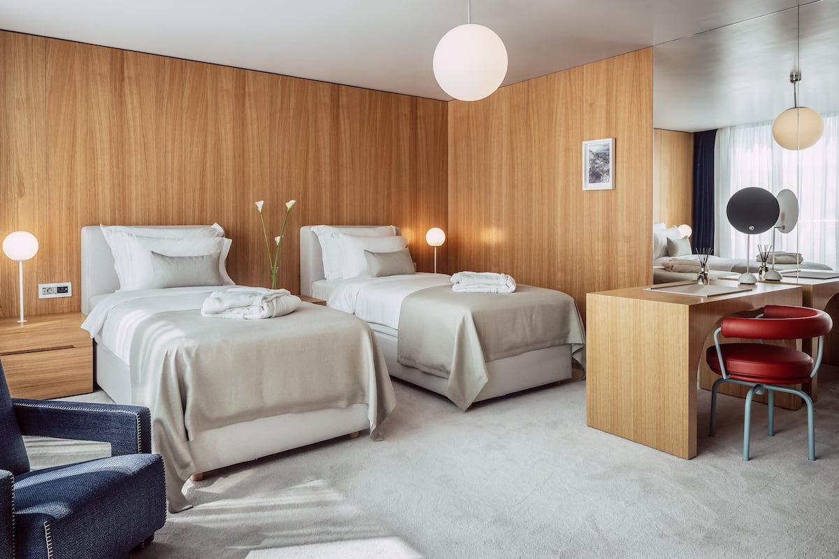 A modern hotel room with two beds, a desk, a chair, and a large mirror.