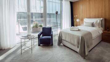 Una habitación de hotel moderna con un ventanal grande, una cama, una silla y una mesita.