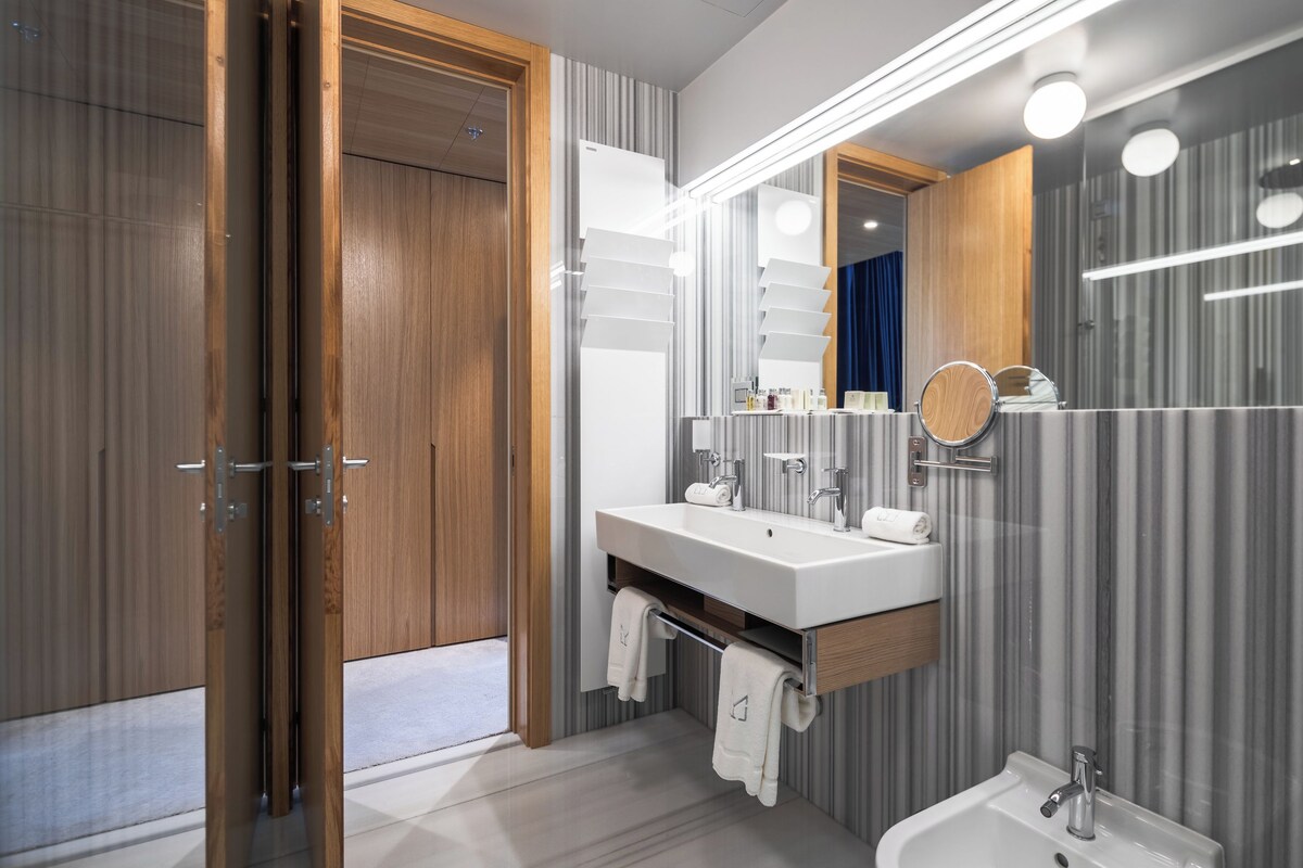 A modern bathroom with a wooden door, a large mirror, a sink, and a bidet.