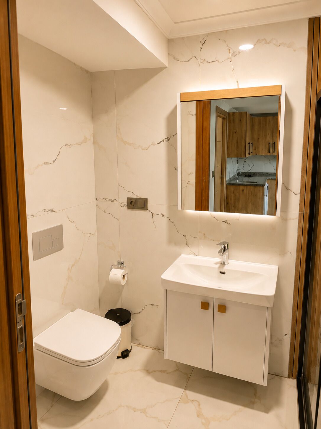 A bathroom with a toilet, sink, mirror, and marble walls.