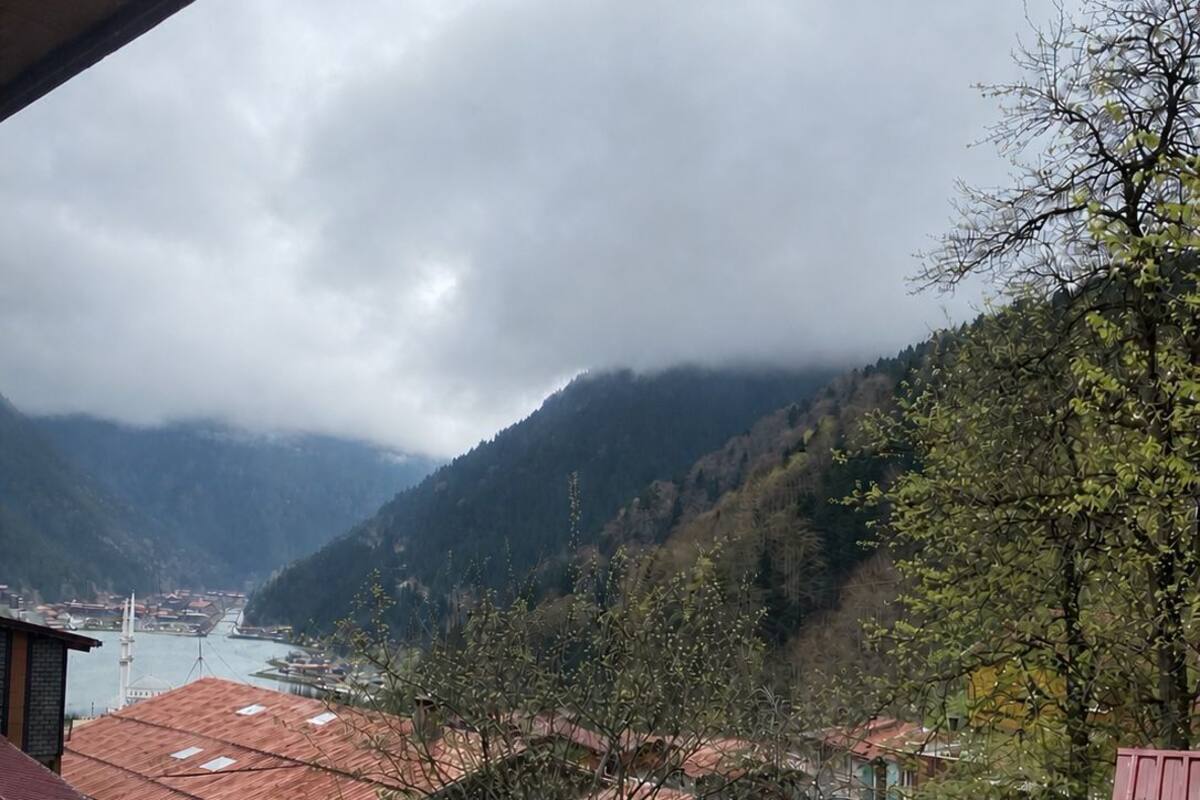 A view of a mountainous landscape with a river, buildings with red roofs, and a paved walkway.