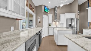 A modern kitchen with white cabinetry, a stainless steel refrigerator, and a large island. - Paradise Point: Beautiful Pool Home in Beachview! (Sanibel)