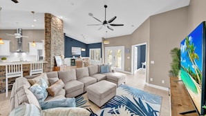 A spacious living room with a large sectional sofa, a kitchen area with white cabinets, and a stone accent wall. - Paradise Point: Beautiful Pool Home in Beachview! (Sanibel)