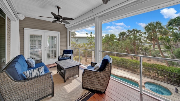 A covered outdoor patio with wicker furniture, a ceiling fan, and a view of palm trees and a swimming pool. - Paradise Point: Beautiful Pool Home in Beachview! (Sanibel)