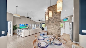 A spacious living area with a dining table set for six, a kitchen with modern appliances, and a large TV screen. - Paradise Point: Beautiful Pool Home in Beachview! (Sanibel)