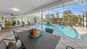 Zona de piscina amb taula, cadires i gandules.