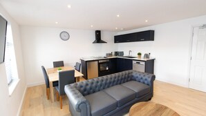 Eine moderne Küche mit Backofen, ein Essbereich mit Tisch und Stühlen sowie ein graues Sofa im Wohnbereich.