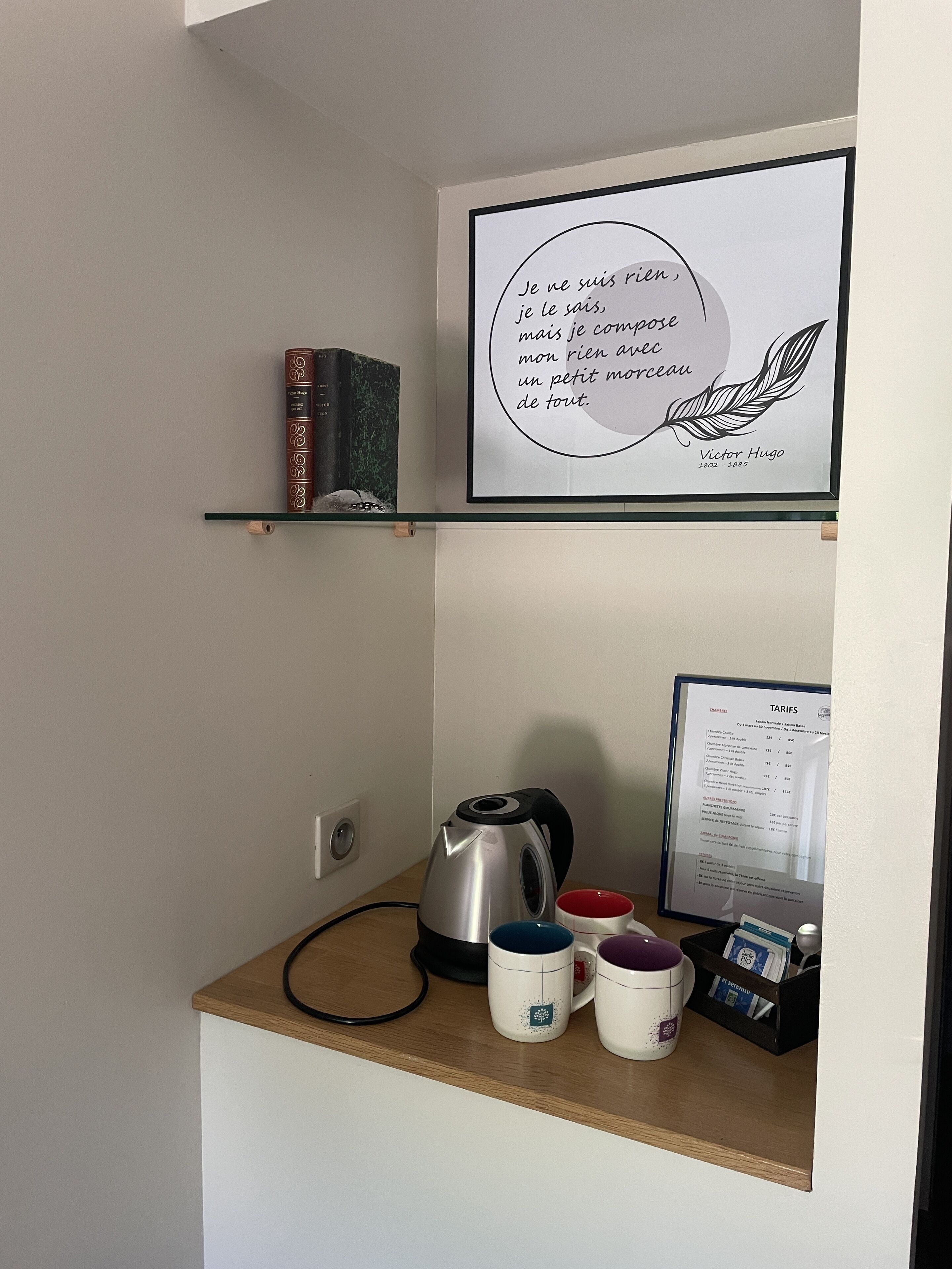 A kitchenette with a kettle, a coffee maker, and a framed quote on the wall.