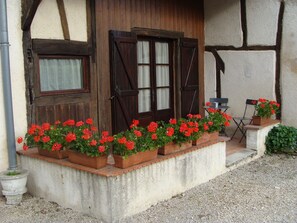 A rustic building with a wooden door and windows, a concrete ledge with flower pots, and a gravel ground. - Inspirations (Saint-Loup-Geanges)