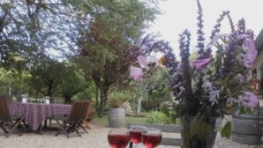 Un área de comedor al aire libre con una mesa preparada para dos, mostrando un plato de pasteles, una copa de vino tinto y un jarrón con flores.