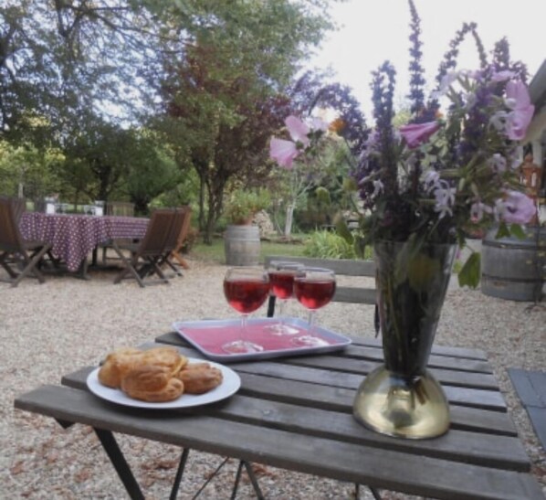 An outdoor dining area with a table set for two, featuring a plate of pastries, a glass of red wine, and a vase with flowers. - Inspirations (Saint-Loup-Geanges)