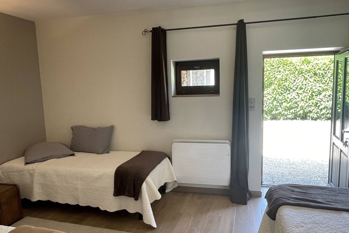 Quarto com cama, janela com cortinas, radiador e vista para o verde lá fora.