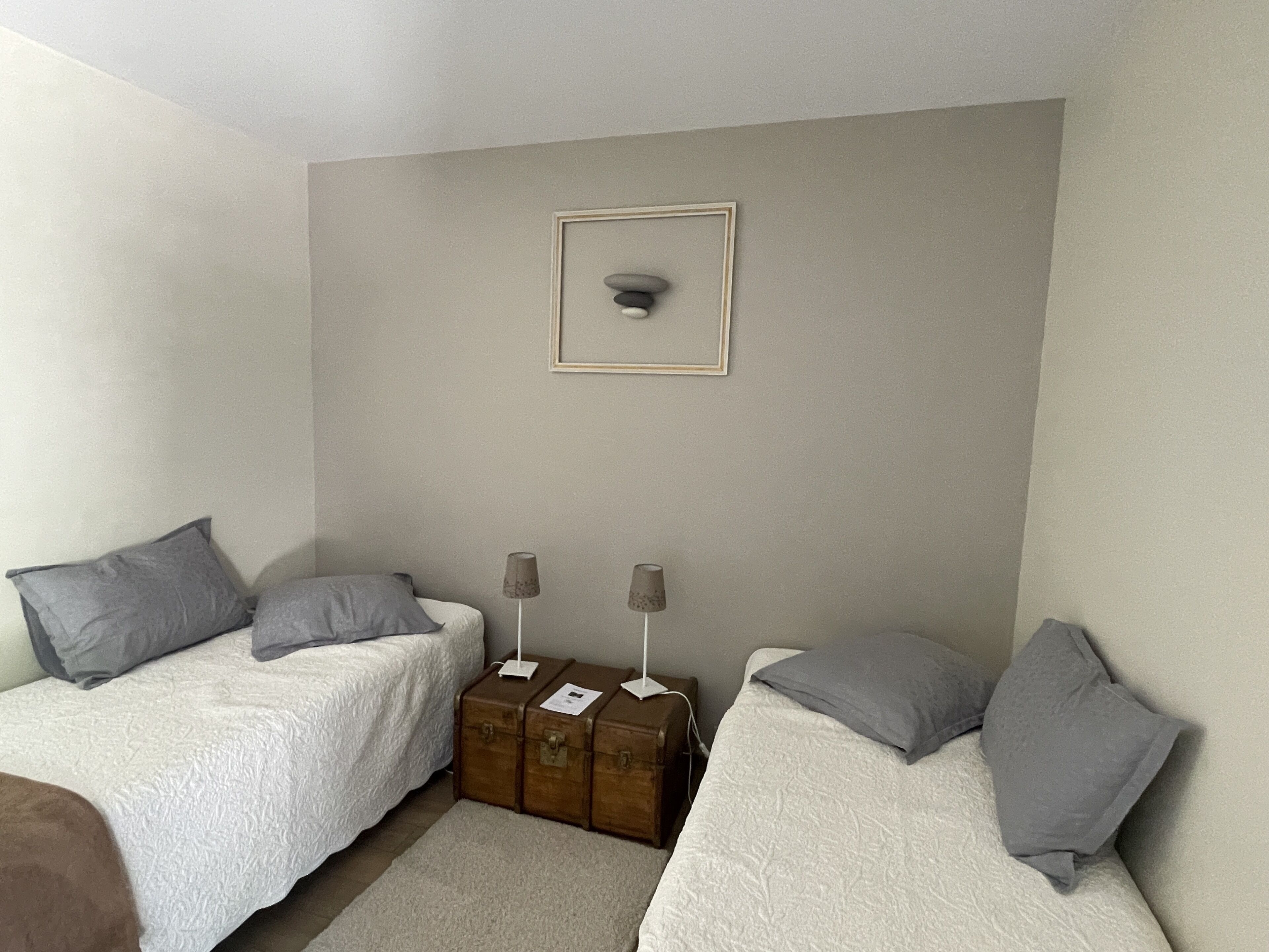 A bedroom with two beds, grey pillows, a framed picture on the wall, and two bedside lamps.