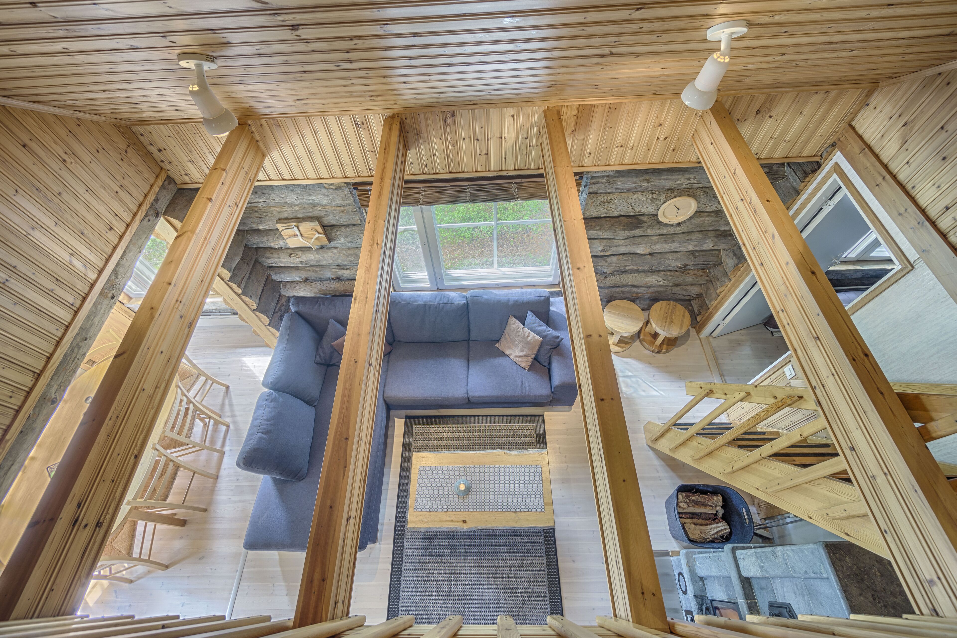 L’intérieur d’une cabane en rondins, avec un canapé bleu, des poutres en bois, une fenêtre et une cheminée.