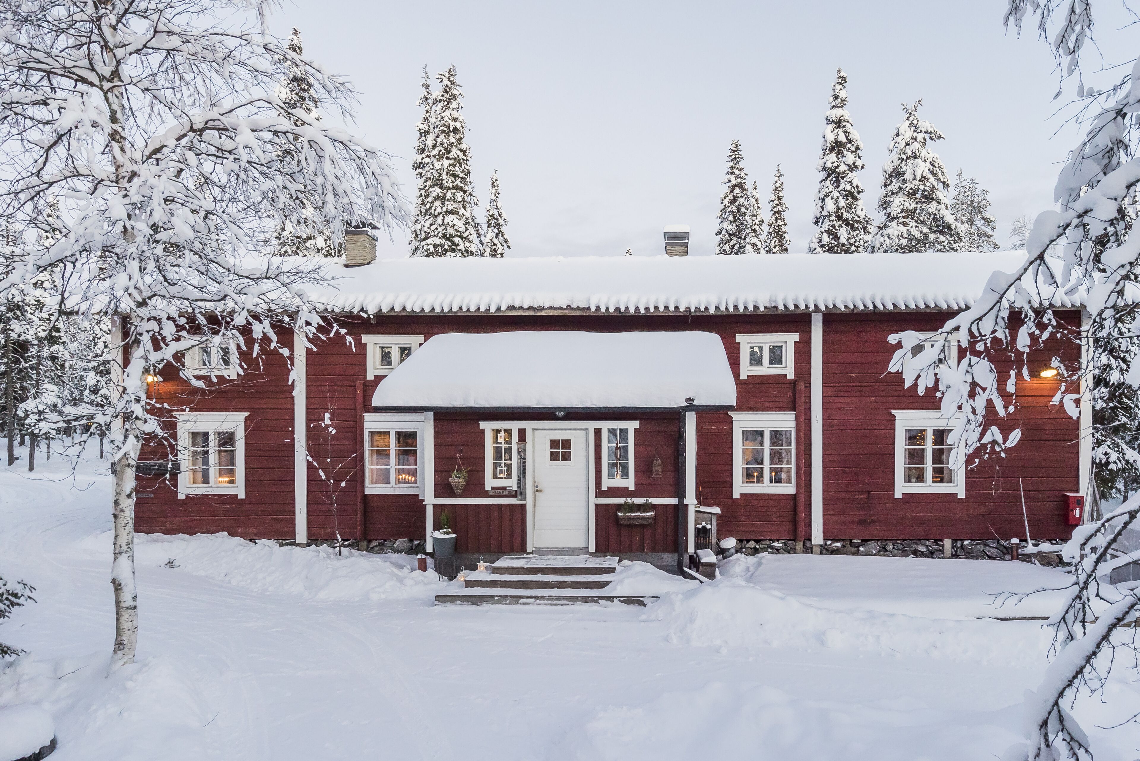 A red wooden house with a snow-covered roof and steps leading to the front door.