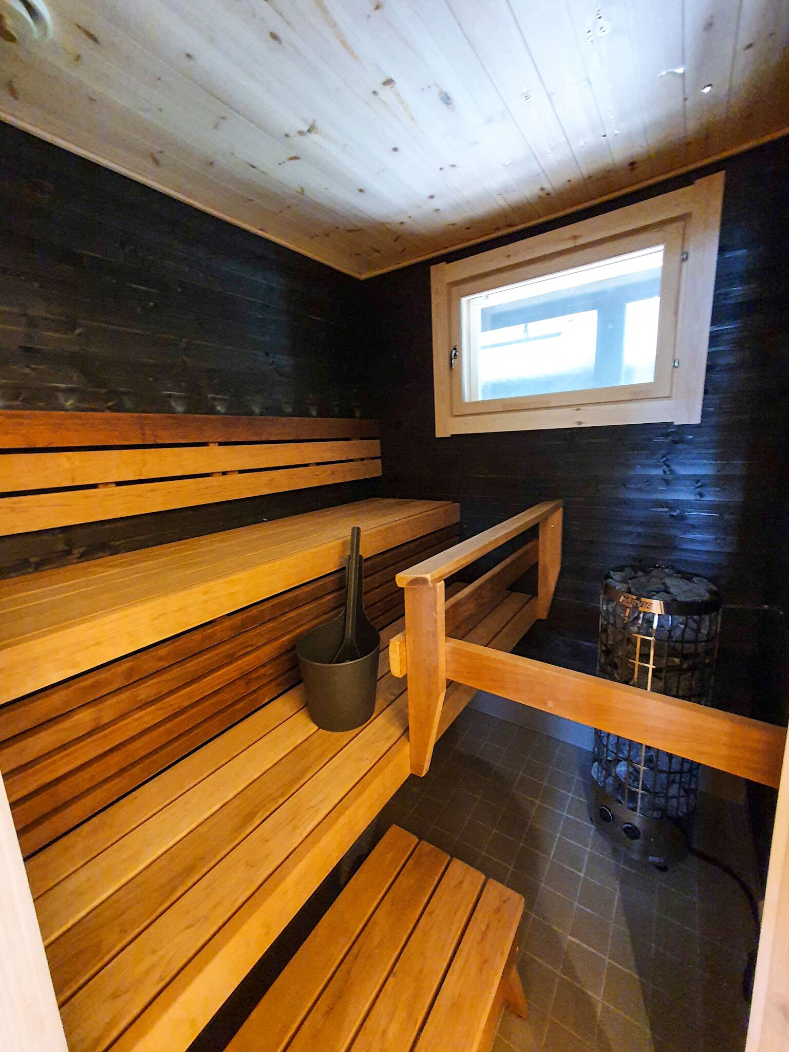 A sauna with wooden benches, a black bucket, and a stone heater.