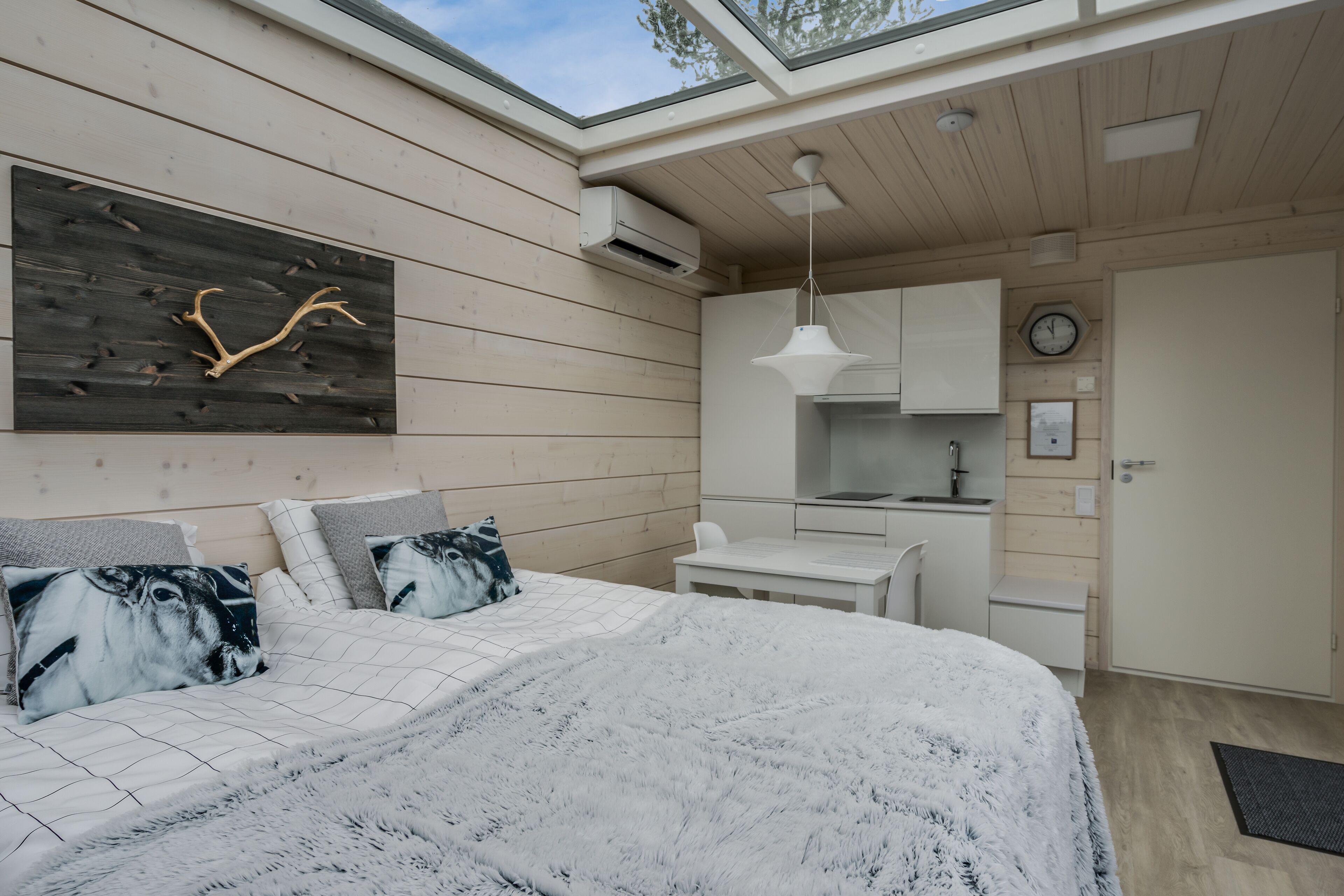 Un dormitorio moderno con una cama grande, un panel de pared de madera, una pequeña kitchenette y un tragaluz.