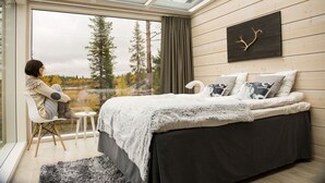 A bedroom with a large window, a bed with a dark bedspread, and a wall-mounted artwork.