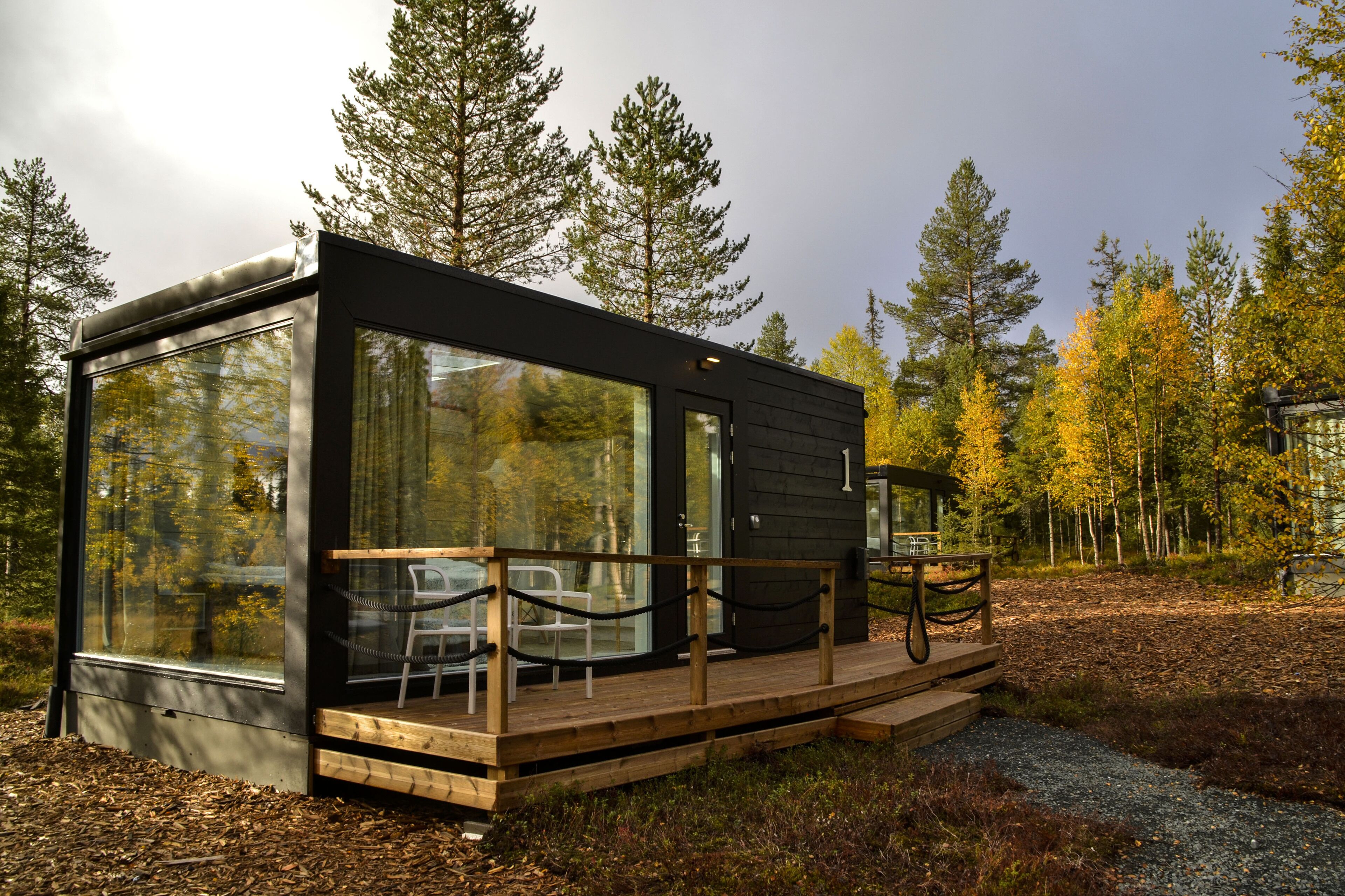 Una cabaña moderna con amplios ventanales, una terraza de madera y un comedor.