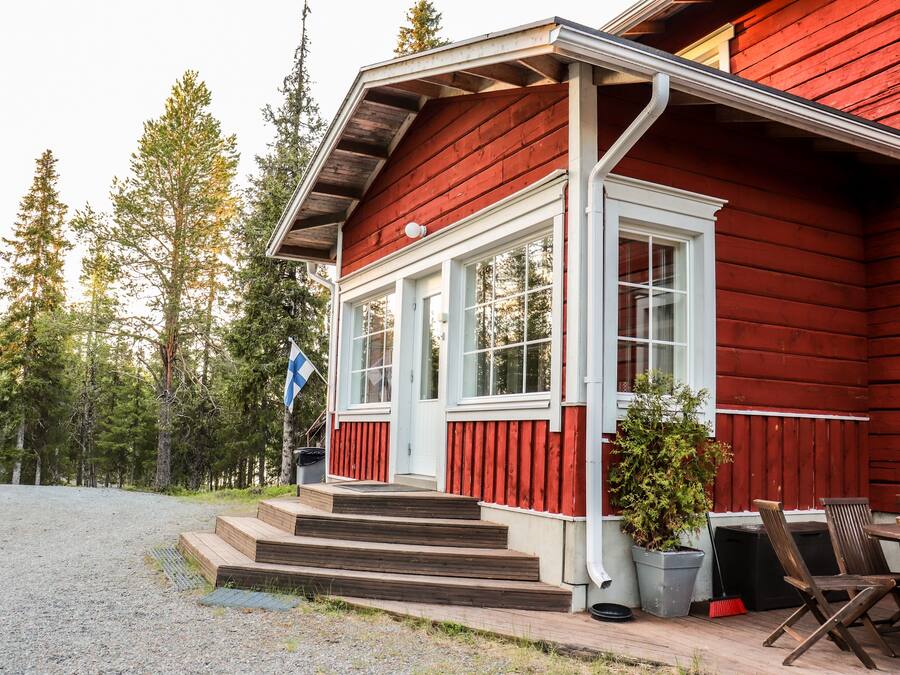 Een houten huis met een rode gevel, witte details en een overdekte veranda met treden die naar de ingang leiden.