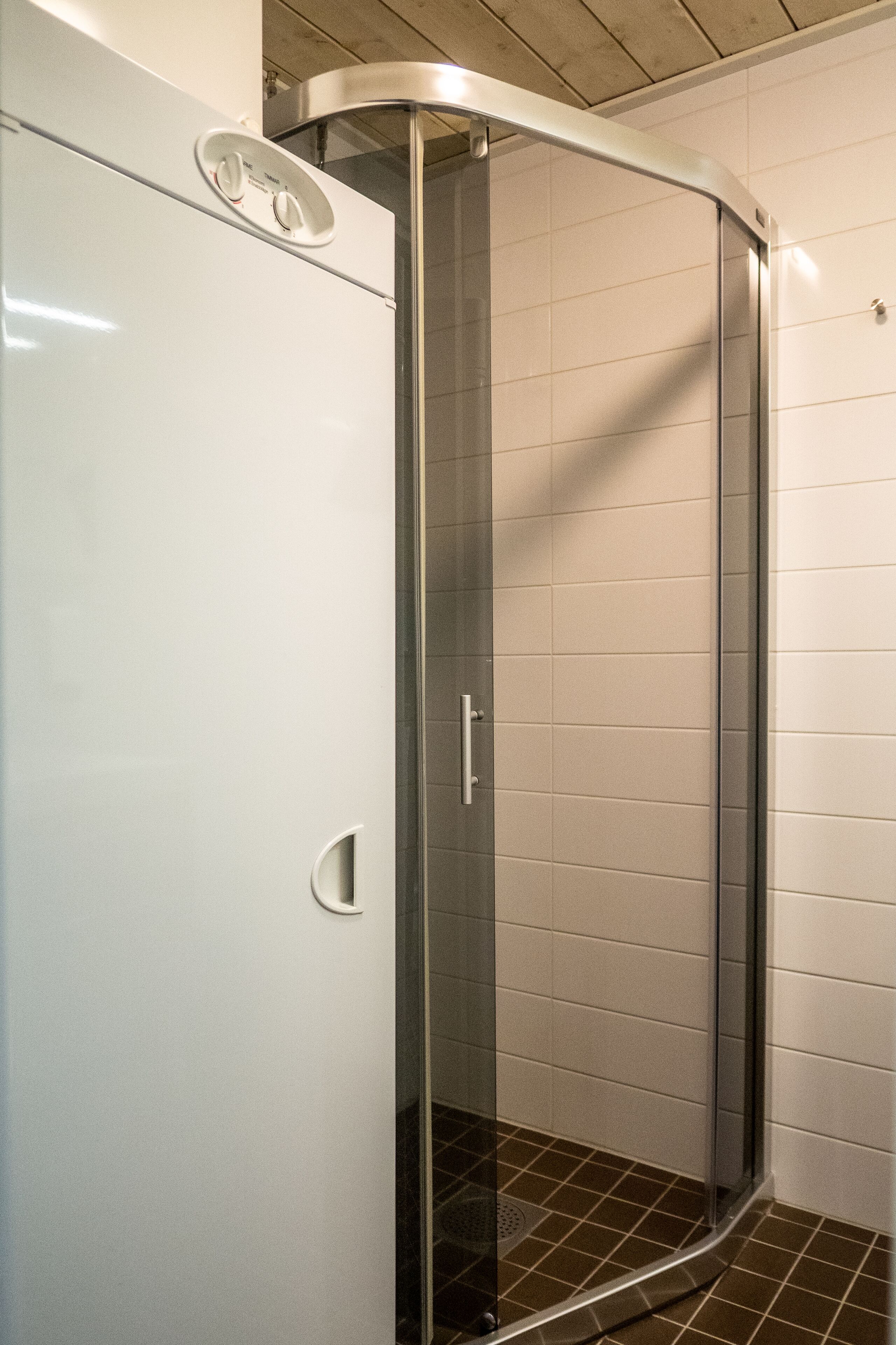 A corner shower with a glass door and a white tiled wall.